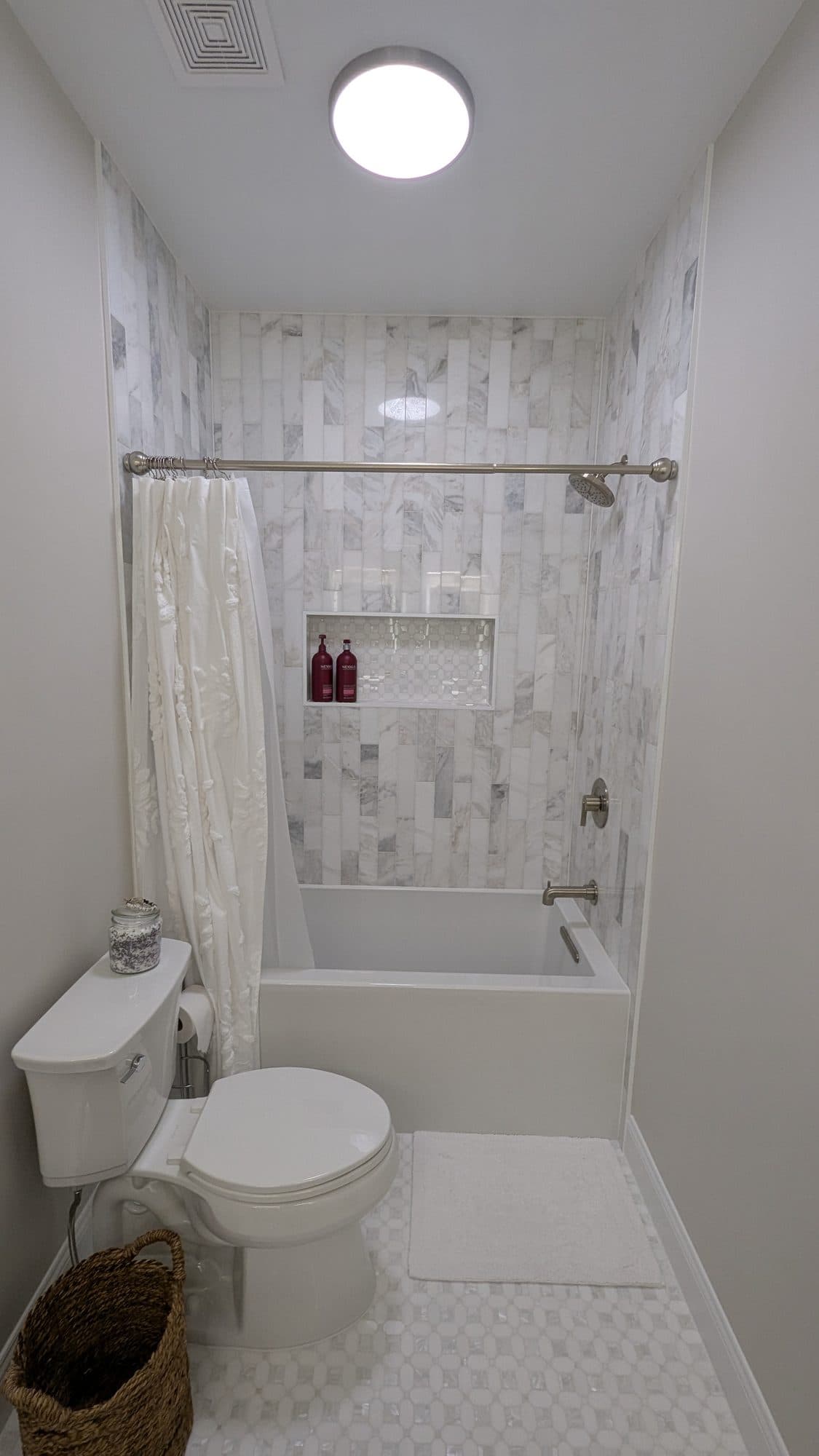 Tub and shower combo with vertical marble tile surround and a built-in niche