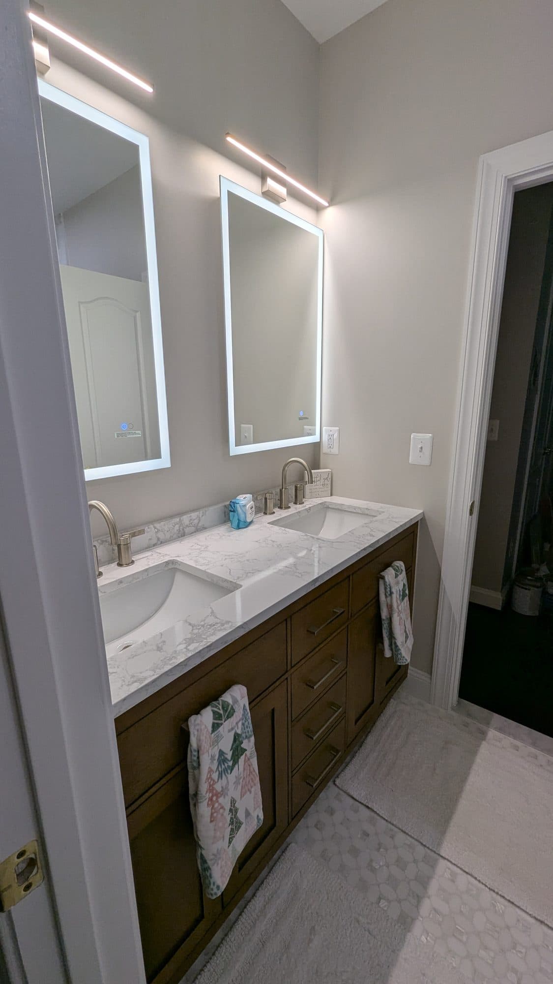 Double vanity with backlit mirrors and stained wood cabinetry, wider view